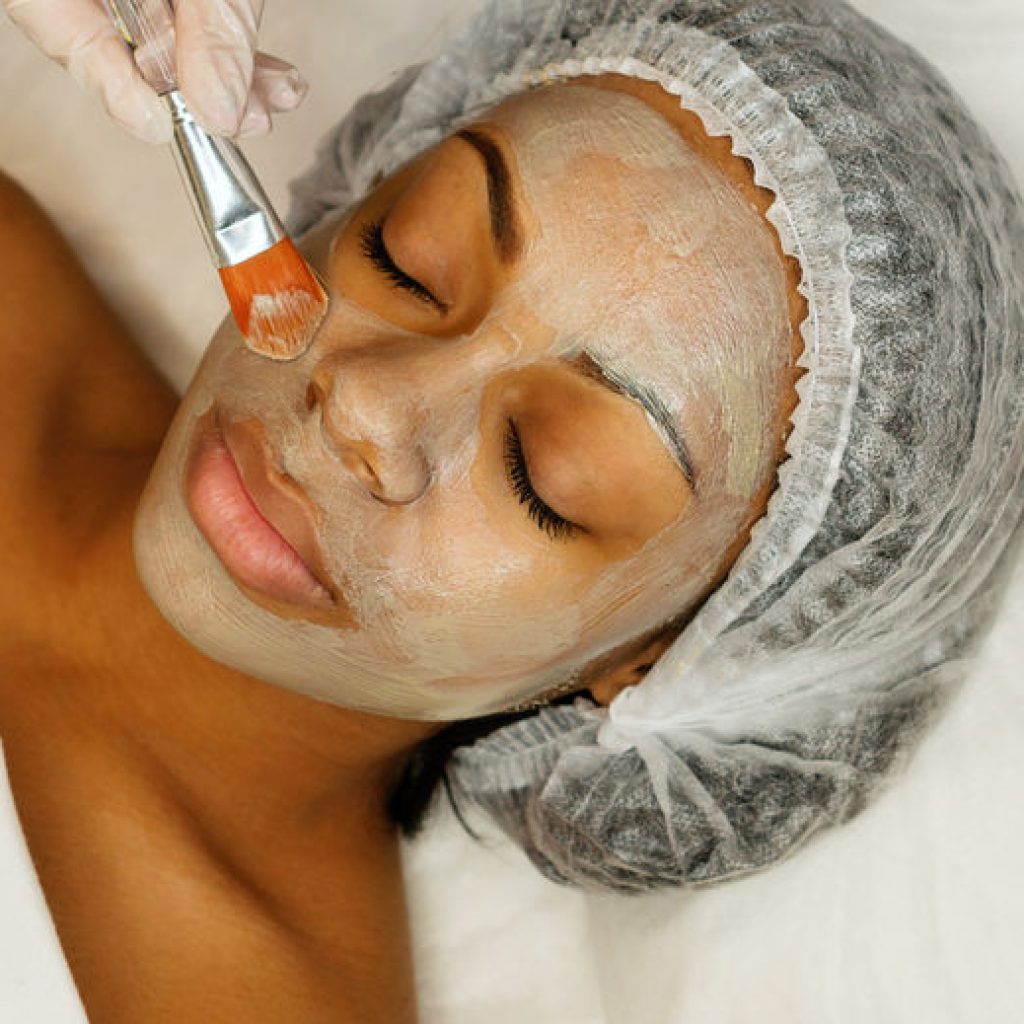 Application of a cosmetology mask on the face of a young afro american woman. Procedure for face skin rejuvenation. Beauty, spa, cosmetology and preservation of youth. Wellness relaxation concept.